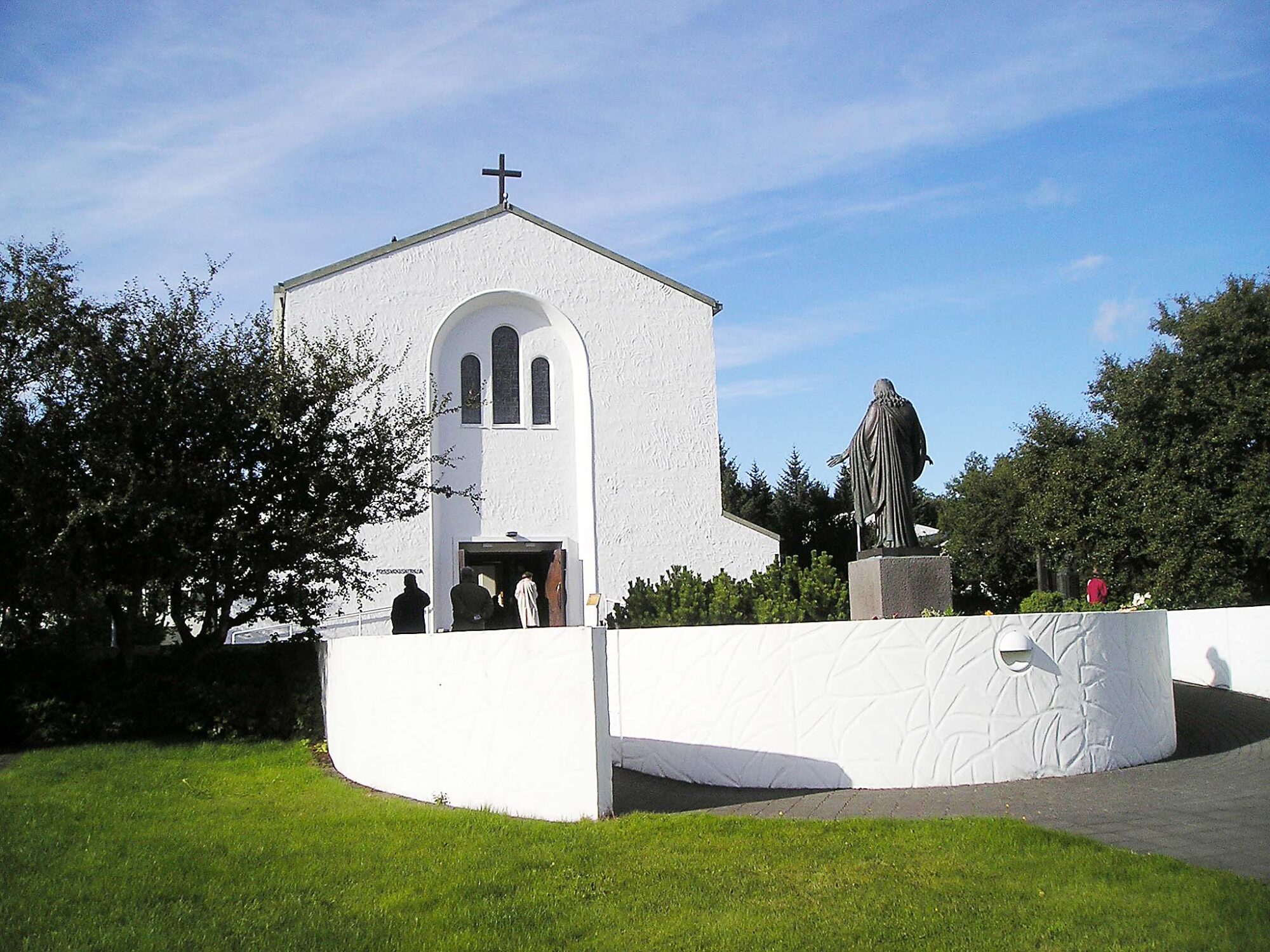 Høy, hvit kirke av mur med en grå statue utenfor.