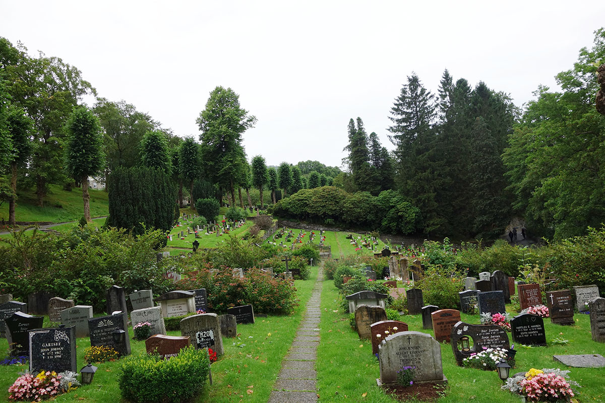 Kirkegård og gravstener omringet av grønt gress og grønne trær.